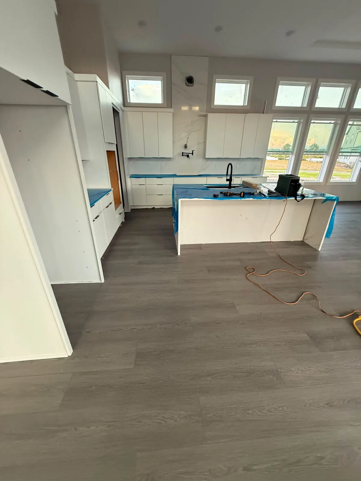 Gray vinyl plank flooring installed around a kitchen island that is still protected with tape