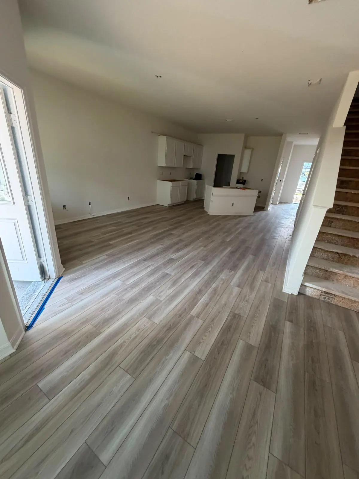 Gray wood-look vinyl plank flooring running through an open living area toward the kitchen and stairs