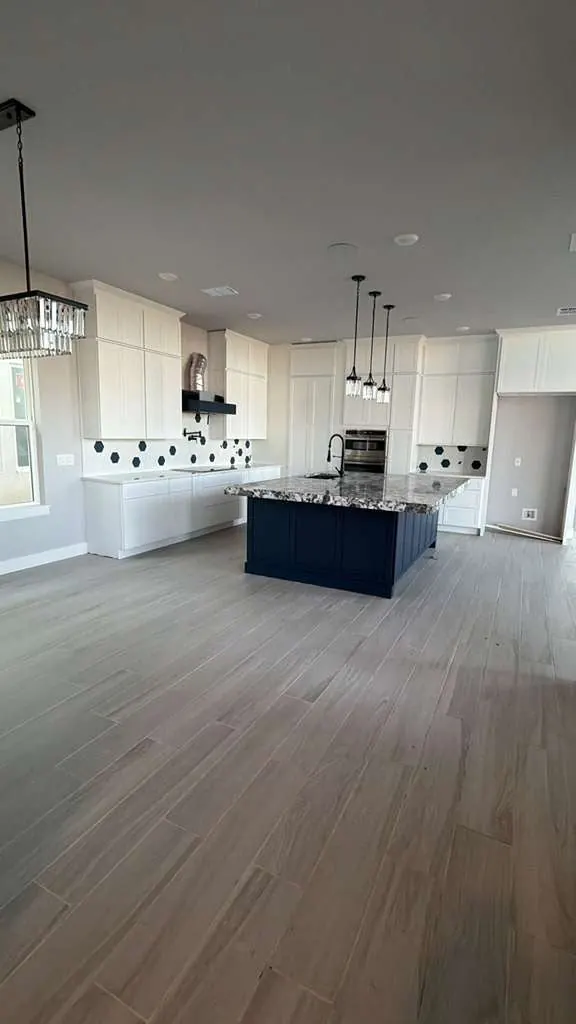 Gray wood-look plank flooring in a large open kitchen with white cabinets and a navy island
