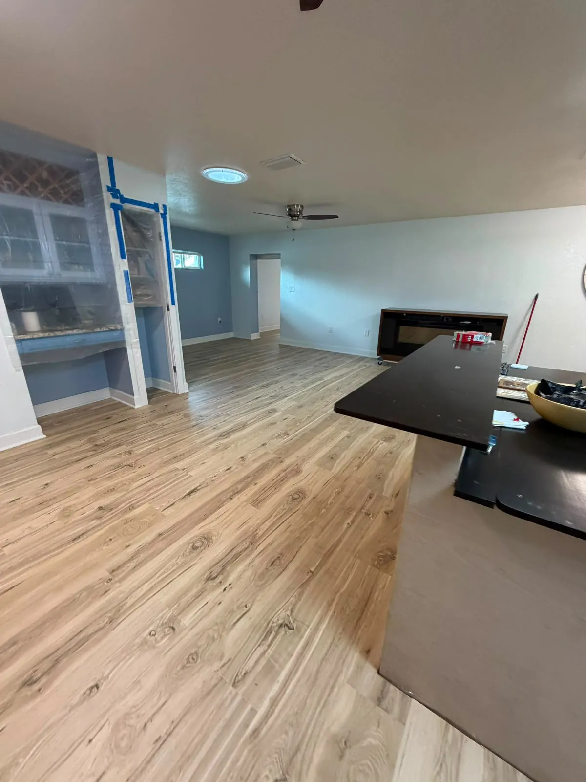 Light wood-look vinyl plank flooring in a living area next to a dark kitchen counter during renovation