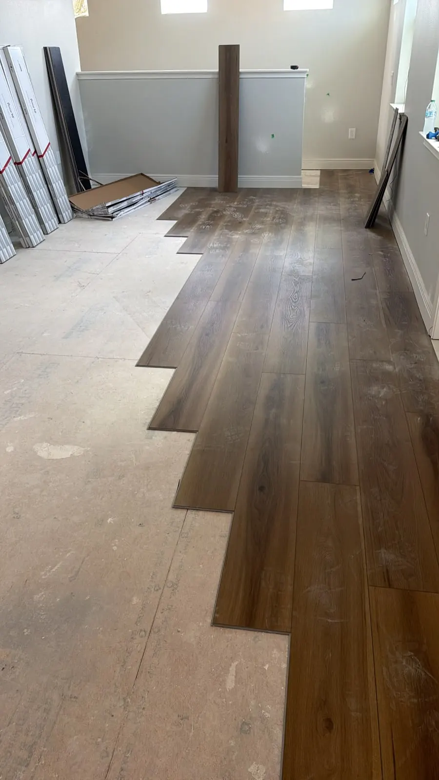 Dark wood-look plank flooring partly installed across a room, with the bare subfloor still visible