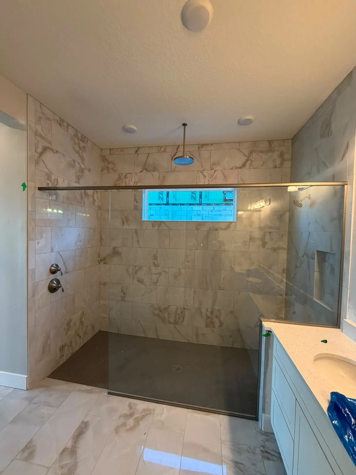 Walk-in shower with marble-look wall tile, a dark shower floor and a glass panel